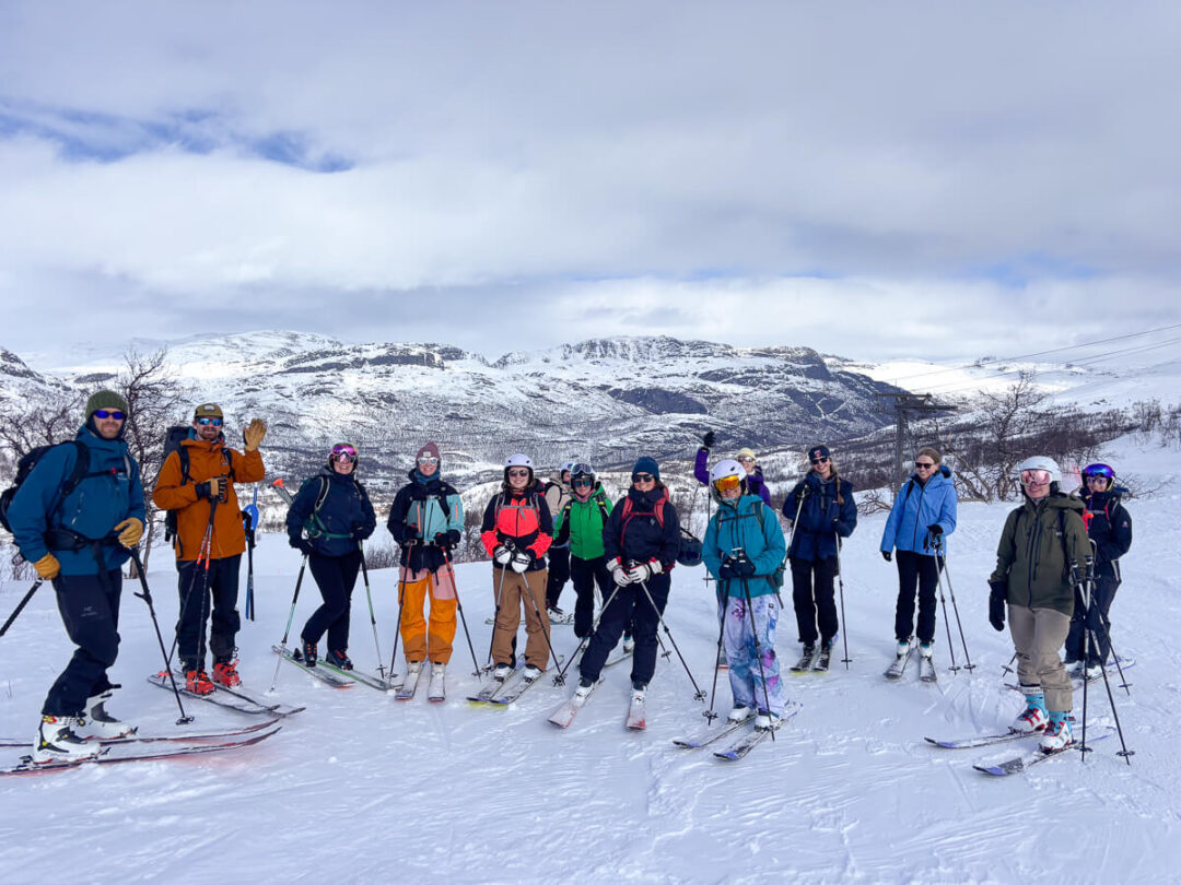 Women ski touring with skis and backpacks on a snowy mountain slope under cloudy skies