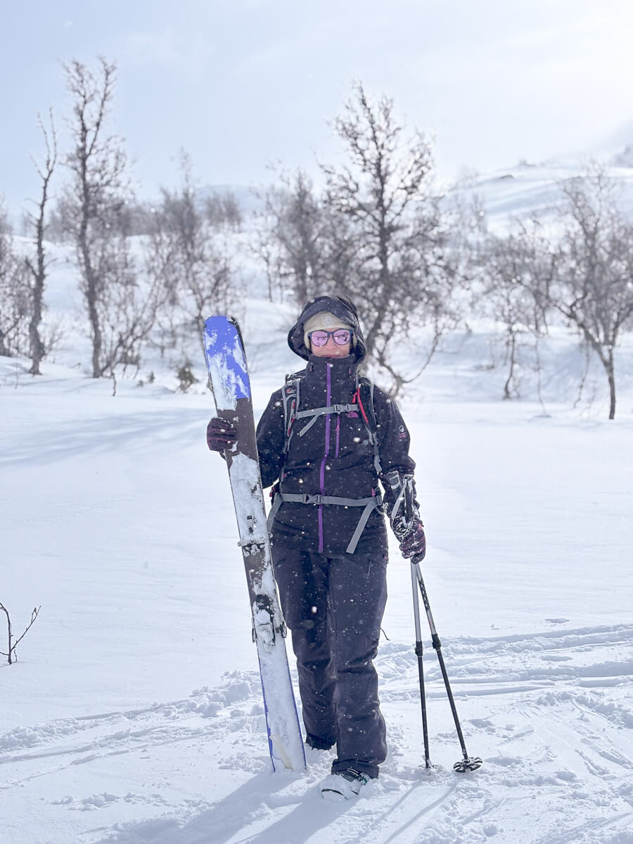 Women ski touring in snowy mountain landscape, holding skis and poles in fresh snow under a cloudy sky