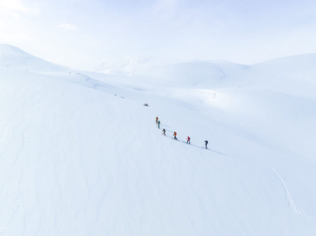Women ski touring across snow-covered mountains in Norway, with a group traversing a wide slope.