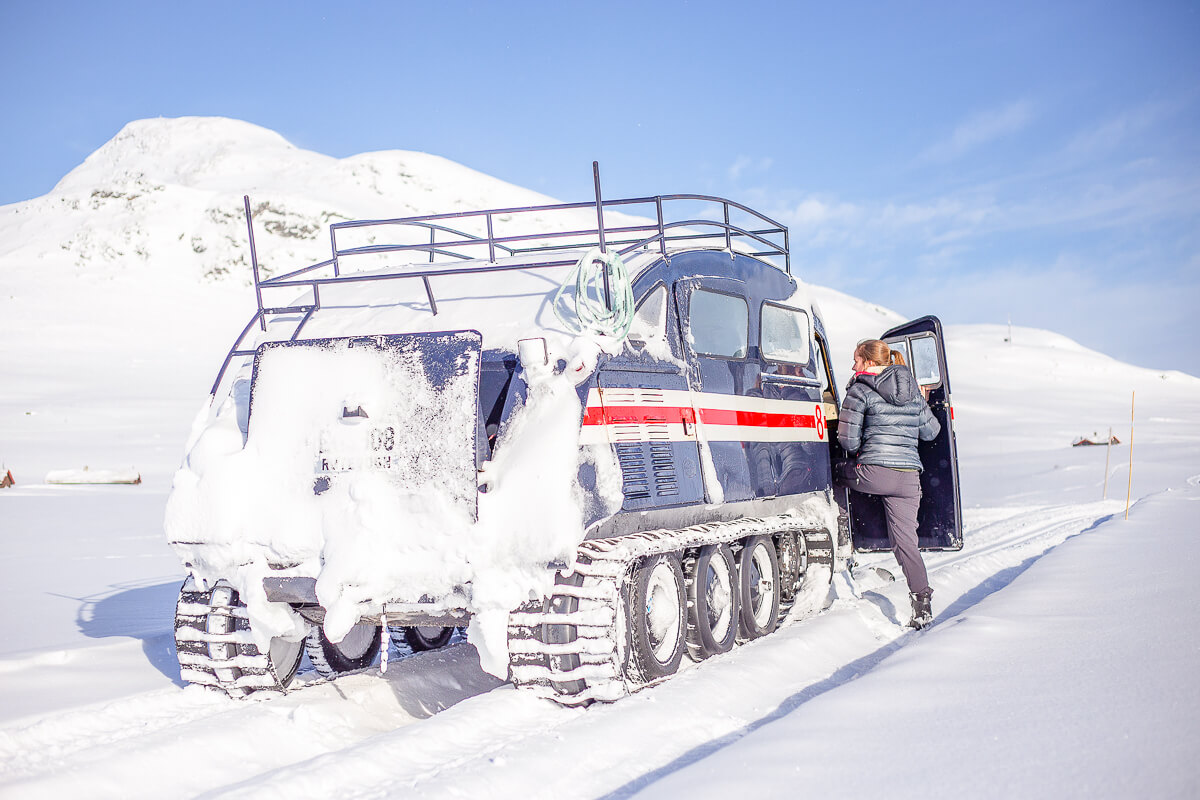 Woman stands beside a snowmobile on a snowy mountain track in winter