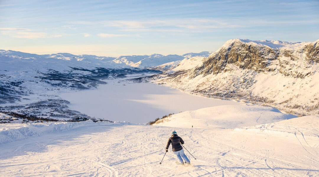 Woman ski touring on snowy mountain slopes overlooking a Norwegian fjord and valleys in winter