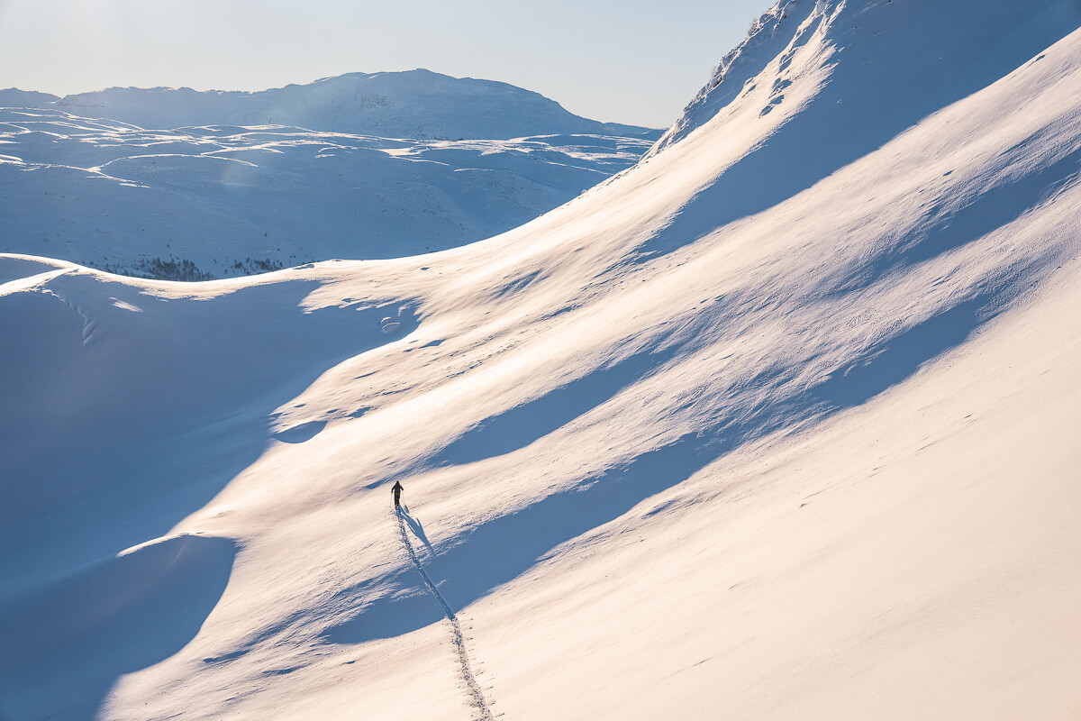 Woman ski touring along a snowy mountain ridge above winter valleys and peaks