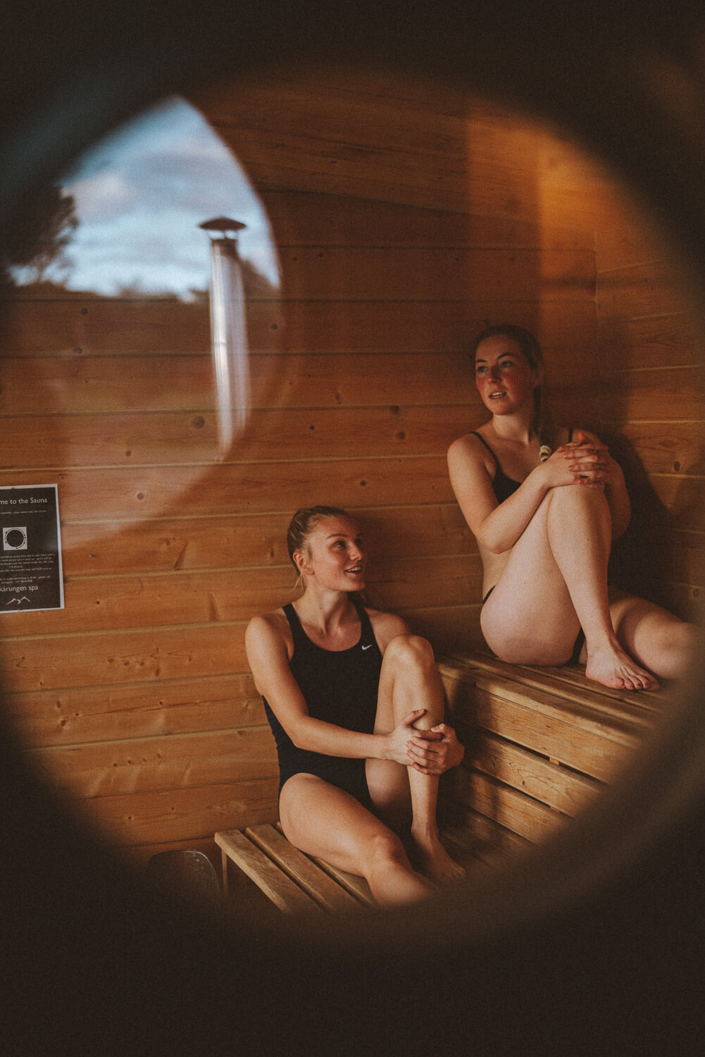 Two women relaxing in a wooden sauna, seated on the bench.