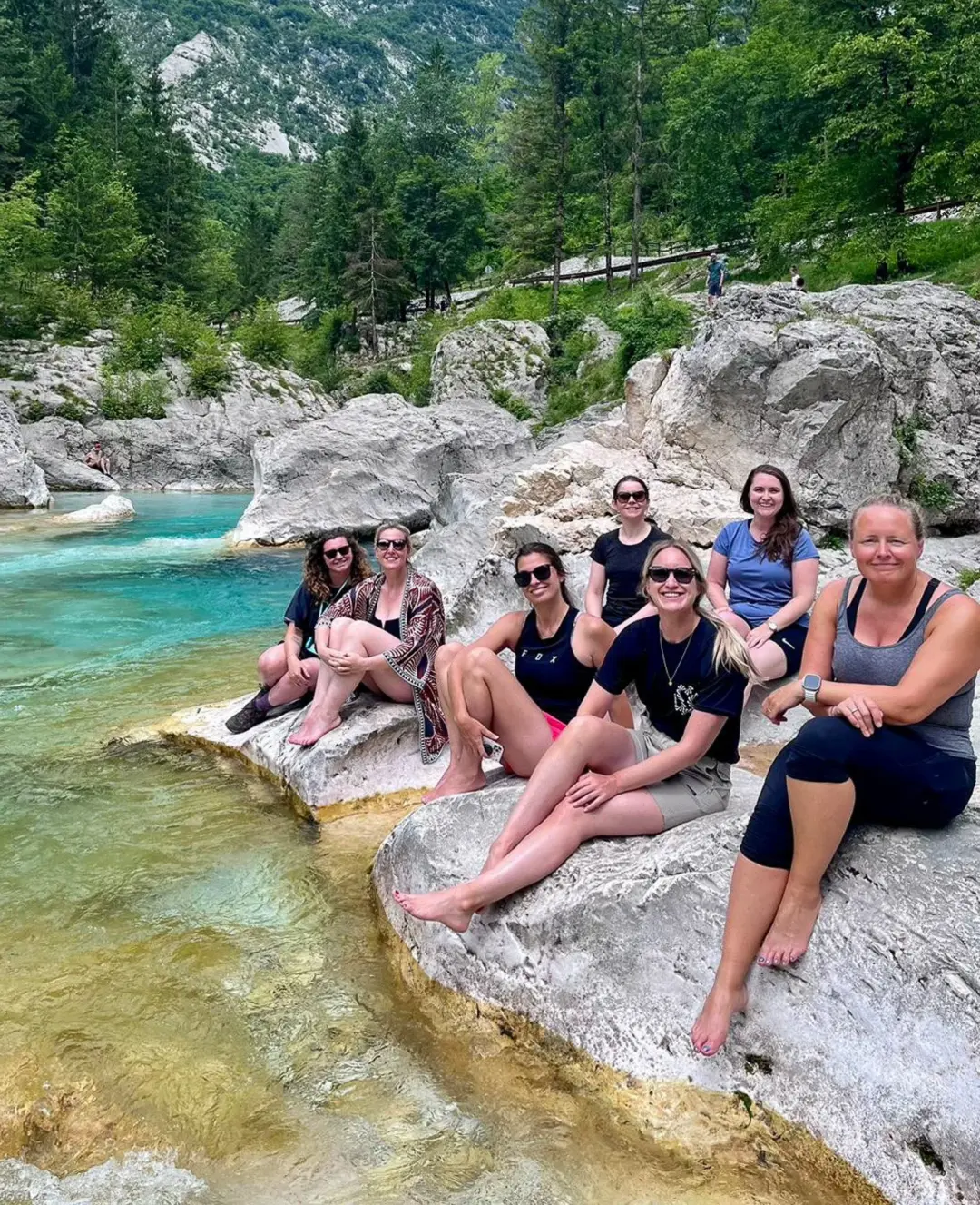 Women hikers sitting on rocks beside a turquoise river in a forested valley