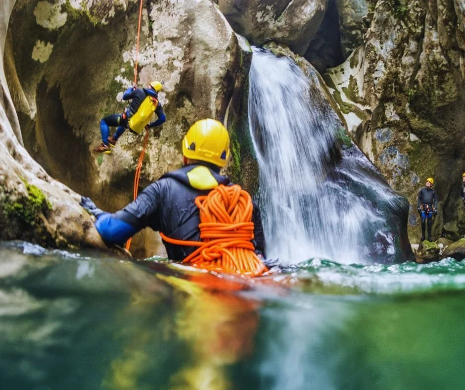 Helmeted paddlers on a whitewater SUP in a rocky canyon beside a waterfall