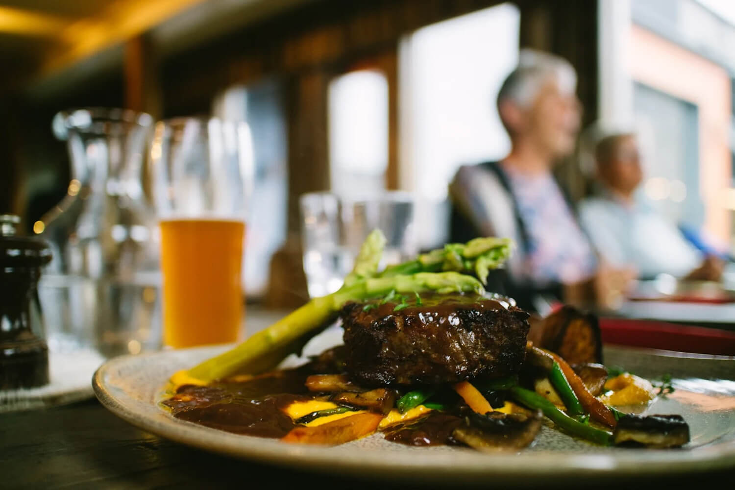 Hearty meal plate with vegetables and sauce in a restaurant, with women dining in the background