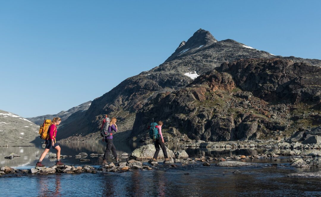 Women hiking on a rocky lake shore with mountains in the background, Norway