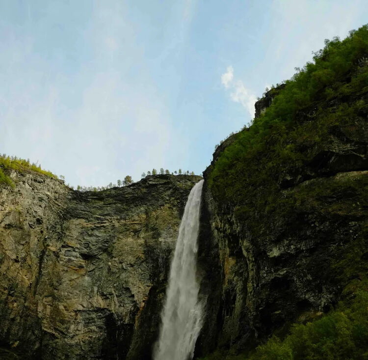 Waterfall in Jotunheimen National Park, Norway, with rocky cliffs and green forest surrounding the falls
