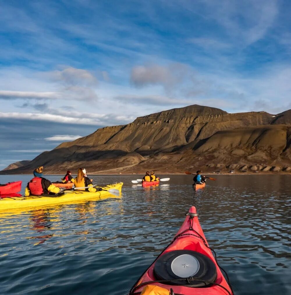 Kayaking on calm water with kayaks in front of rocky mountains in Svalbard, Arctic summer expedition