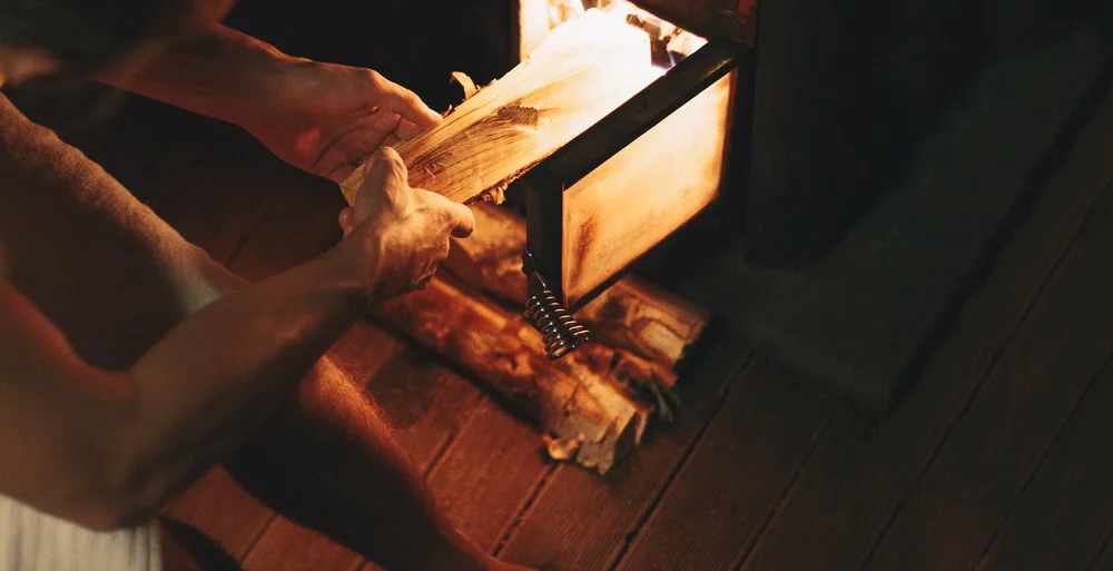Hands tending a sauna heater with glowing embers in a warm steam room