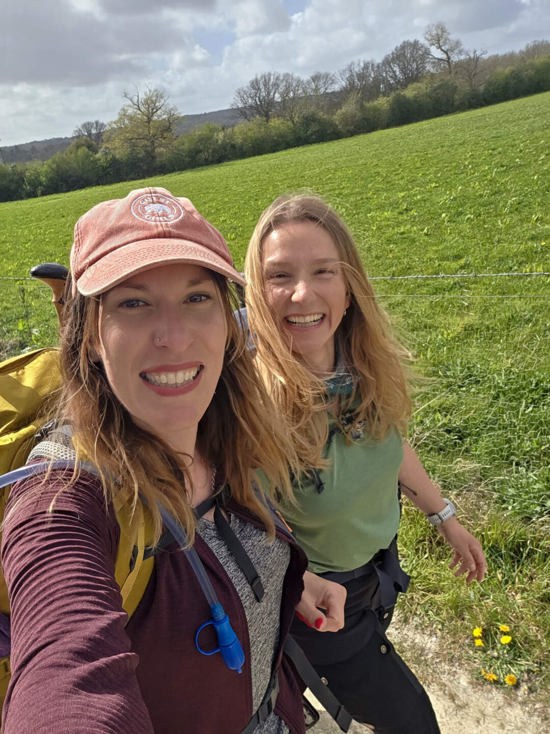 Two women on a day hike in green countryside, smiling while walking along a countryside path.