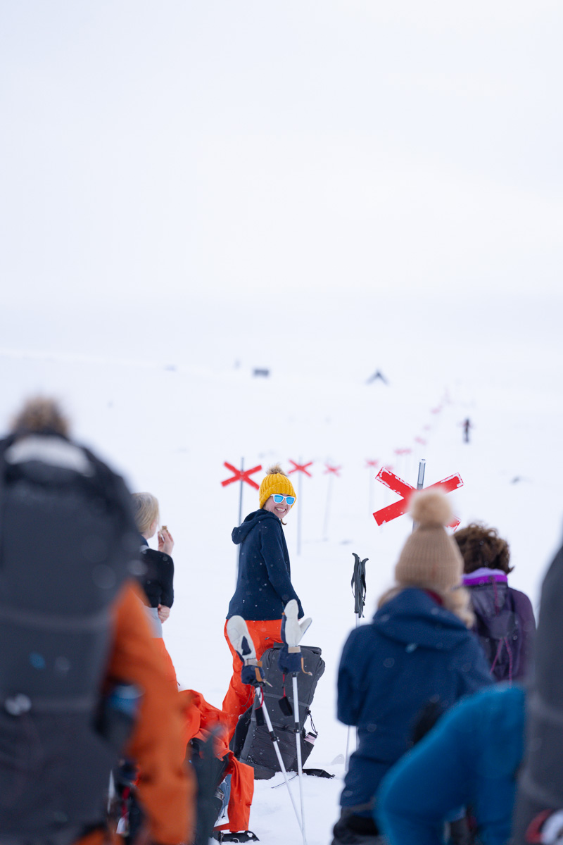 Women skiing on a snowy mountain slope with other skiers watching ahead