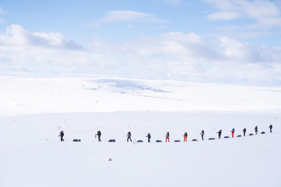 Women trekking across a snowy landscape in winter, with a distant snowy mountain ridge