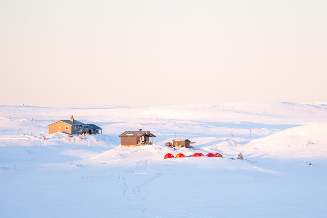 Snow-covered mountain cabins and huts with tents in a white winter landscape at dawn