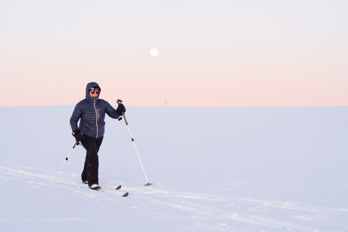 Woman skiing on snowy mountainside at sunrise, wearing skis and poles