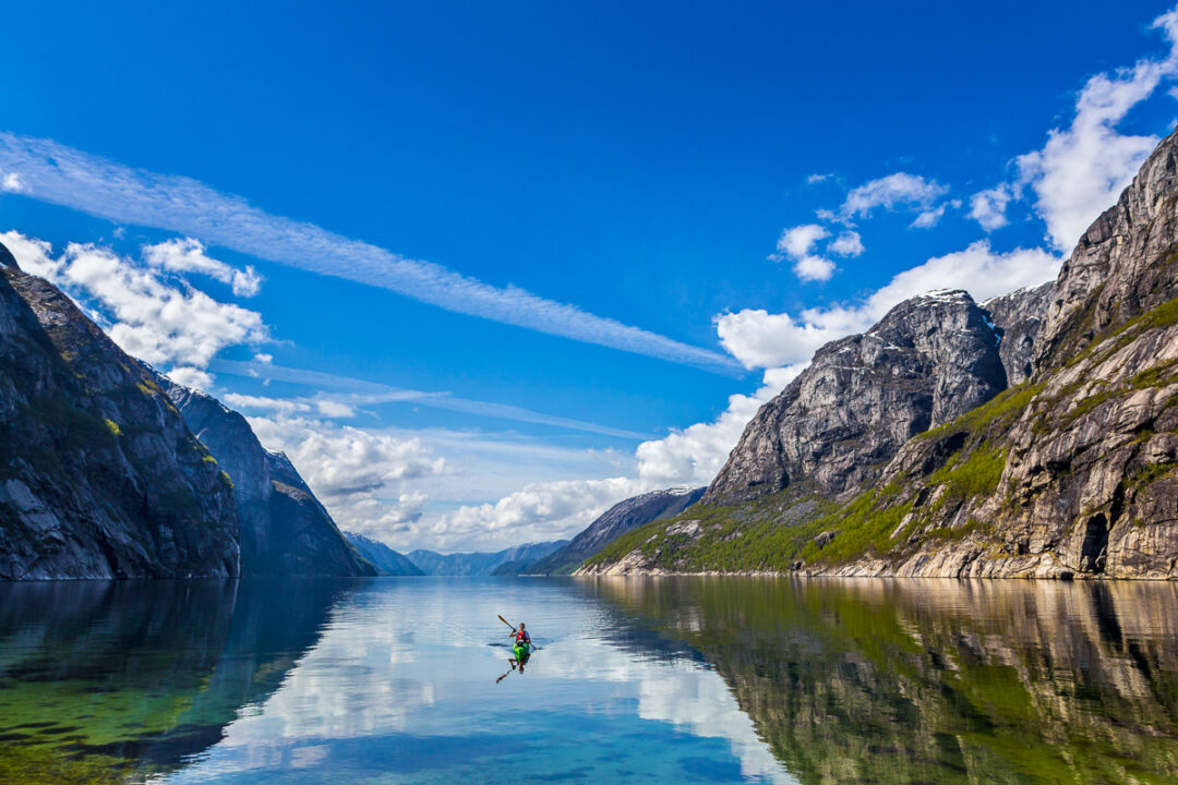 Kayaker paddling on a calm fjord with steep mountains in the distance