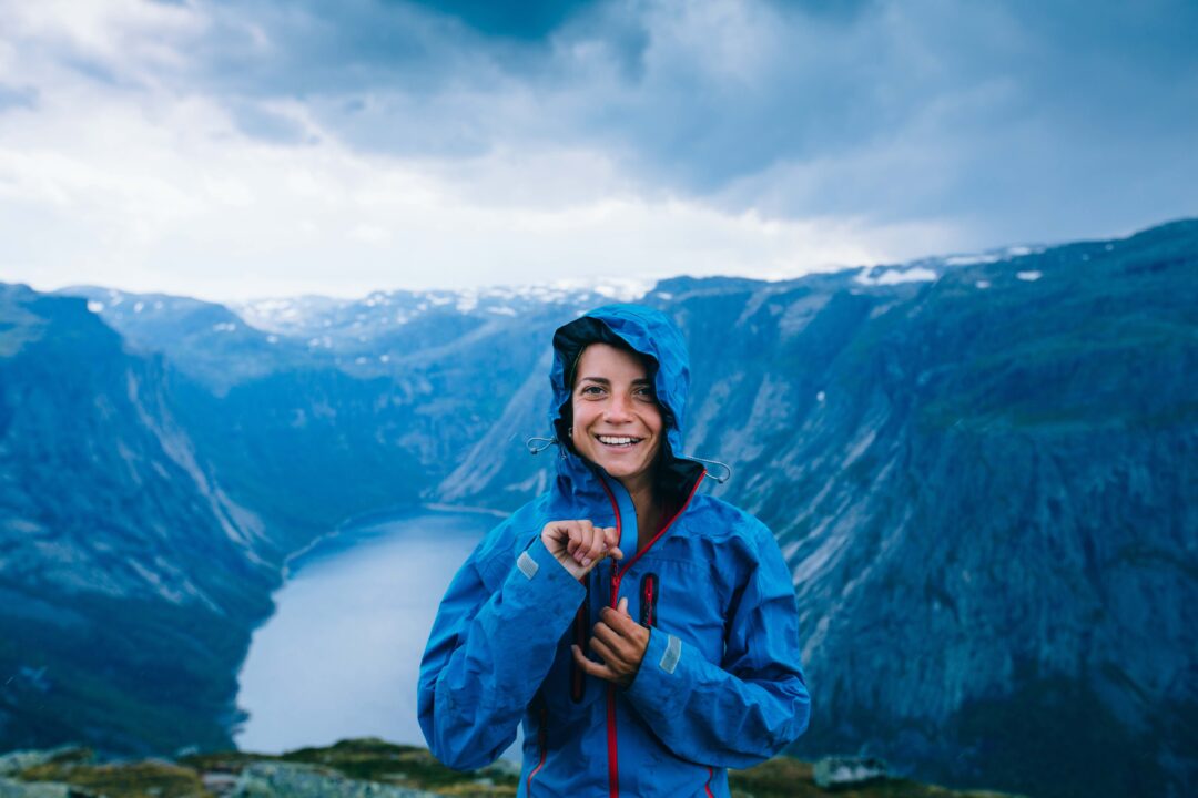 Woman in a blue waterproof jacket smiling in a rainy mountain landscape