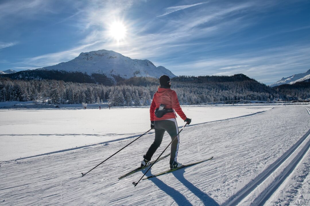 Woman cross-country skiing on a snow-covered frozen lake with mountain peaks and blue sky in winter