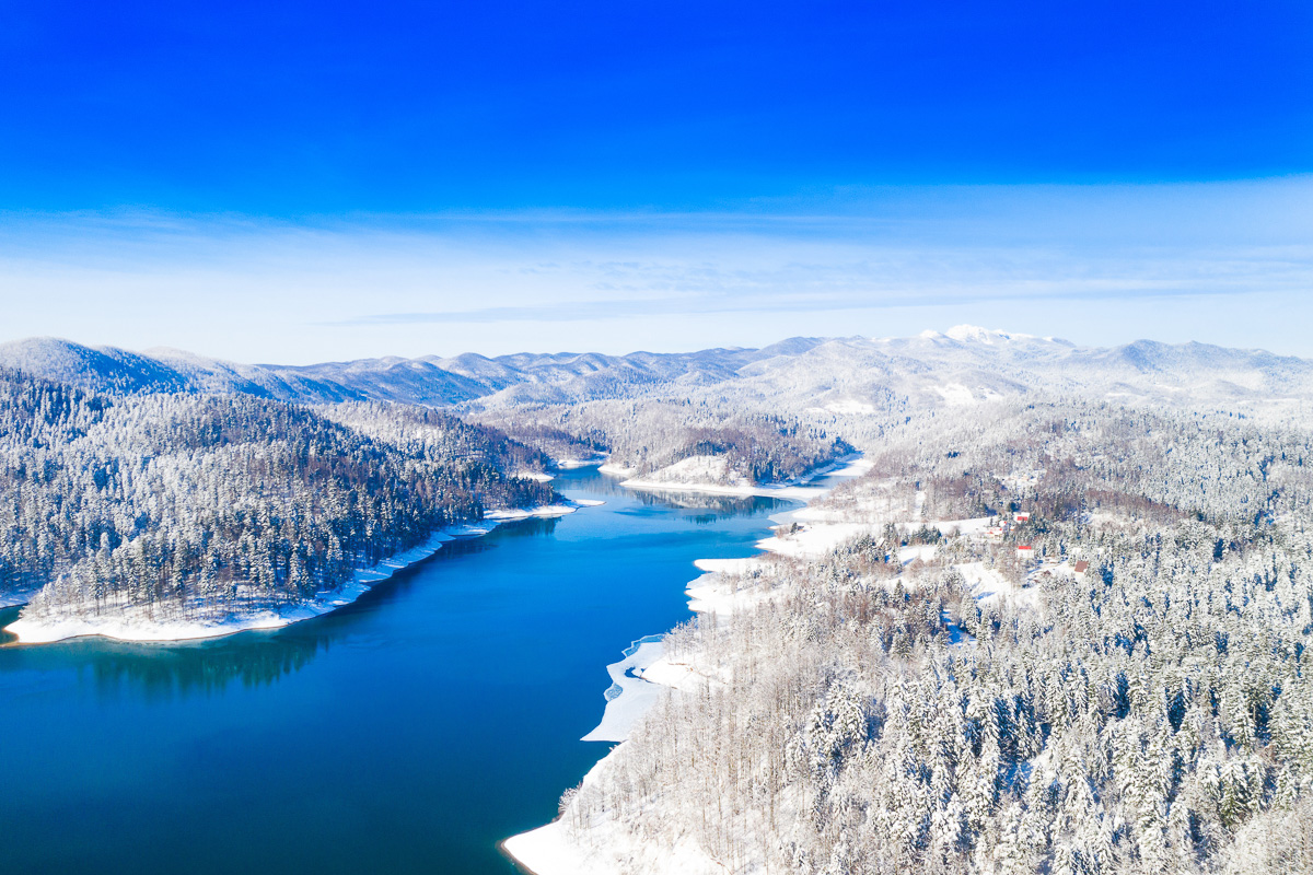 Snow-covered forests and mountains along a winding river in winter, viewed from above