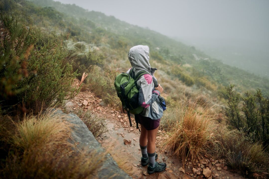 Woman hiking on a misty mountain trail in a hooded rain jacket and backpack