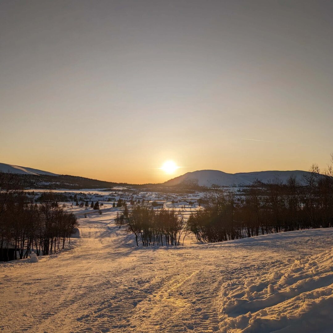 Cross-country ski trail through a snowy valley at sunrise, with hills and trees in spring light