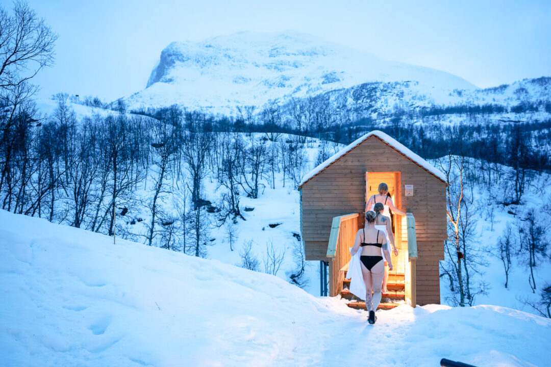 People approaching a sauna cabin in snow.