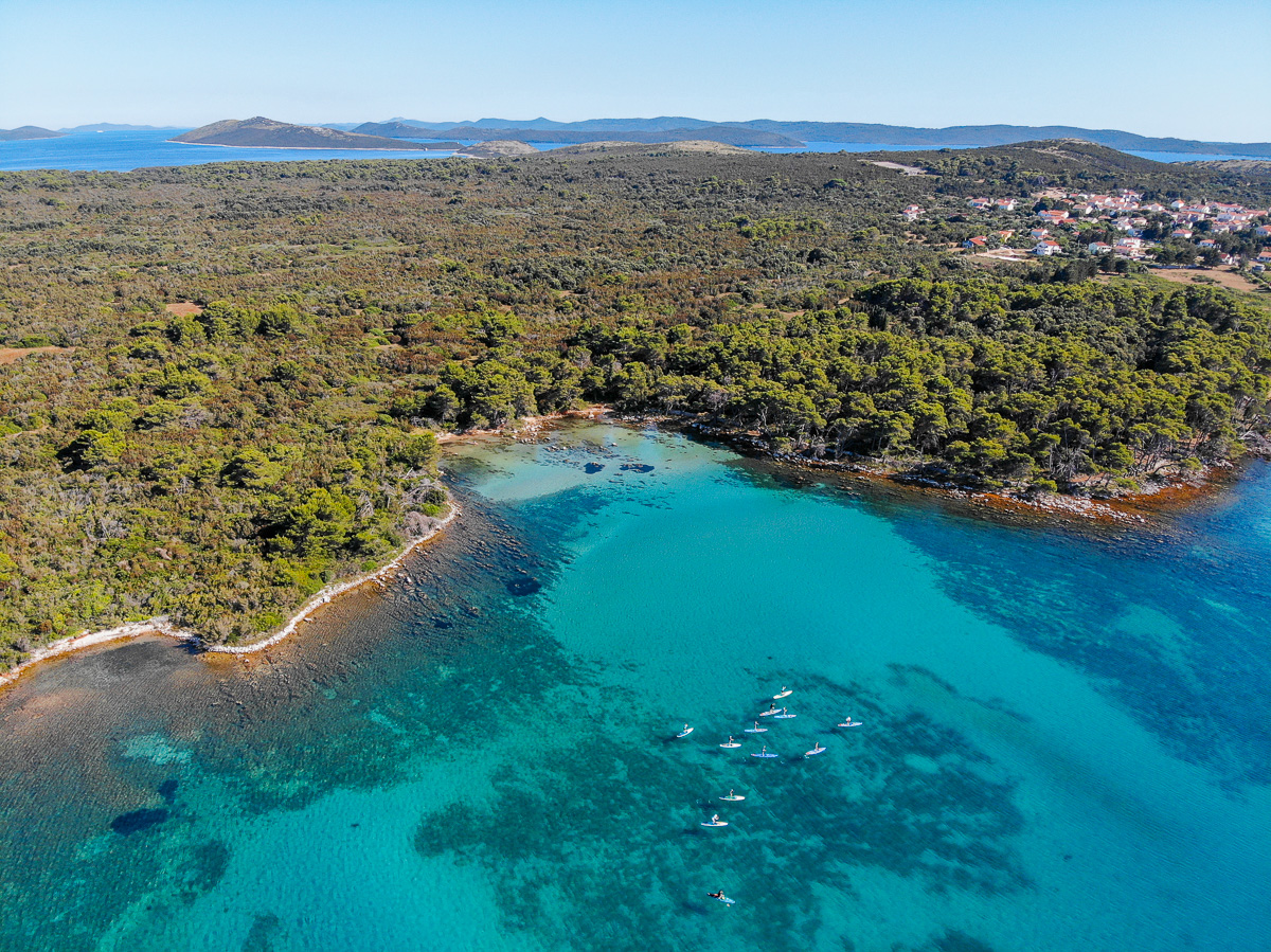 Aerial view of a turquoise bay with boats on calm water, surrounded by green hills and coastline
