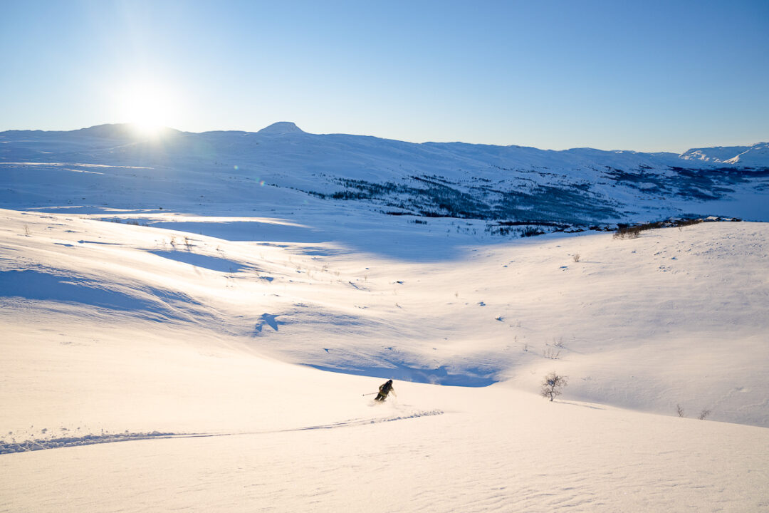 Skier descends a snowy mountain valley in winter sunshine