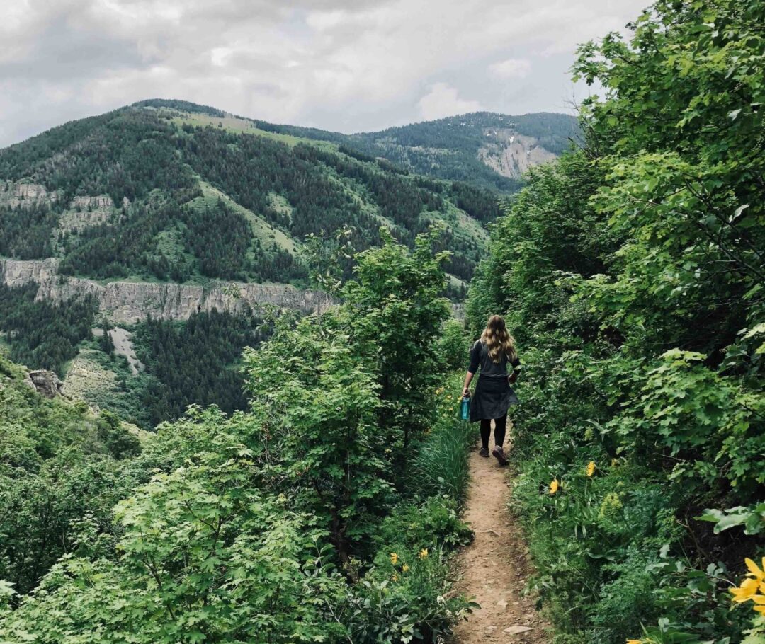 Woman hiking a trail through lush green mountains in a valley outdoors