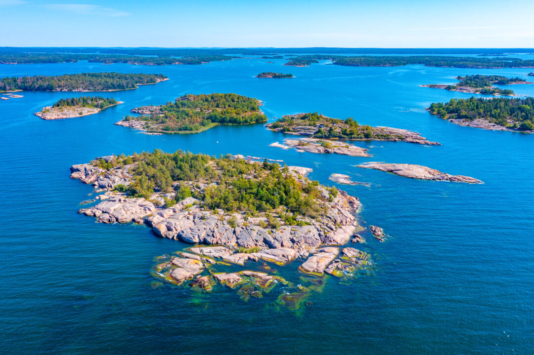 Aerial view of a rocky, forested island with coves in clear blue water