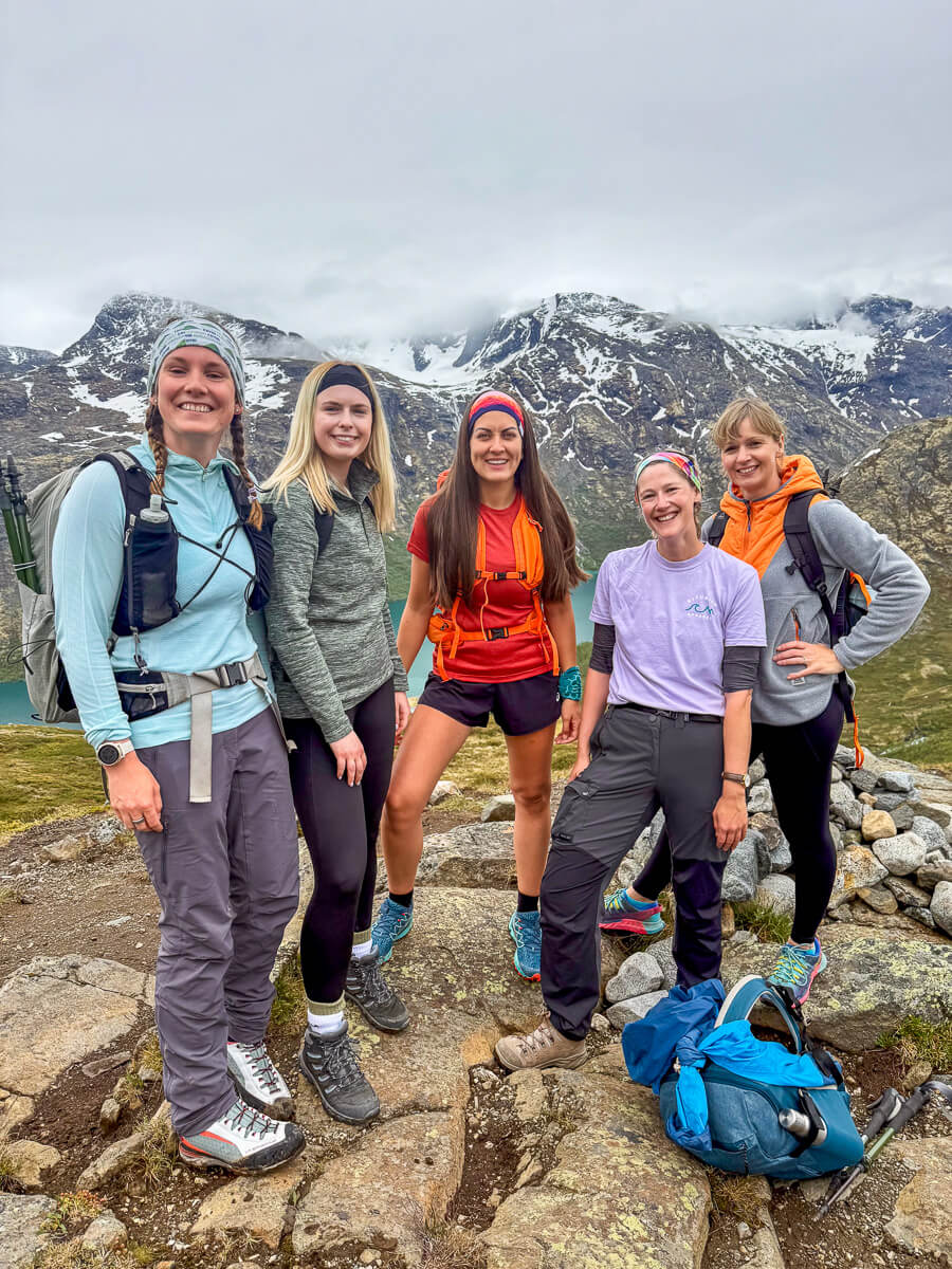 Women hiking on a rocky mountain trail with snowy peaks in the background, outdoors adventure