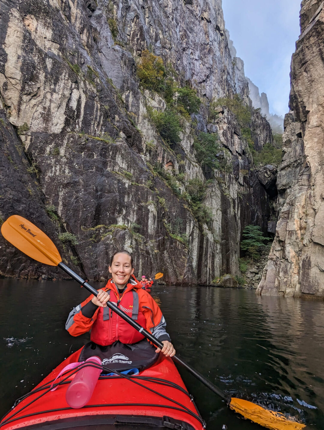Woman kayaking on a calm river through rocky canyon cliffs, adventure holiday outdoor paddling scene