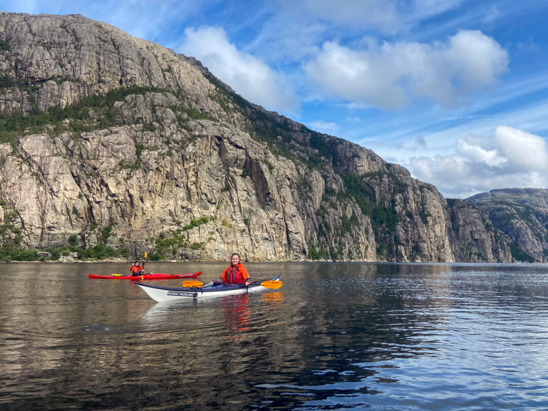 Women kayaking on a calm fjord with steep cliffs in the background, Europe.