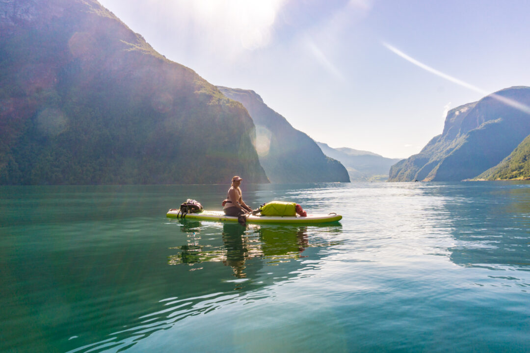 Woman kayaking on a calm lake with towering mountains in the background