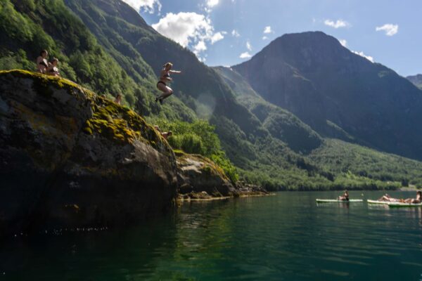 Women hiking on a rocky cliff and kayaking on a mountain lake with alpine peaks in the background