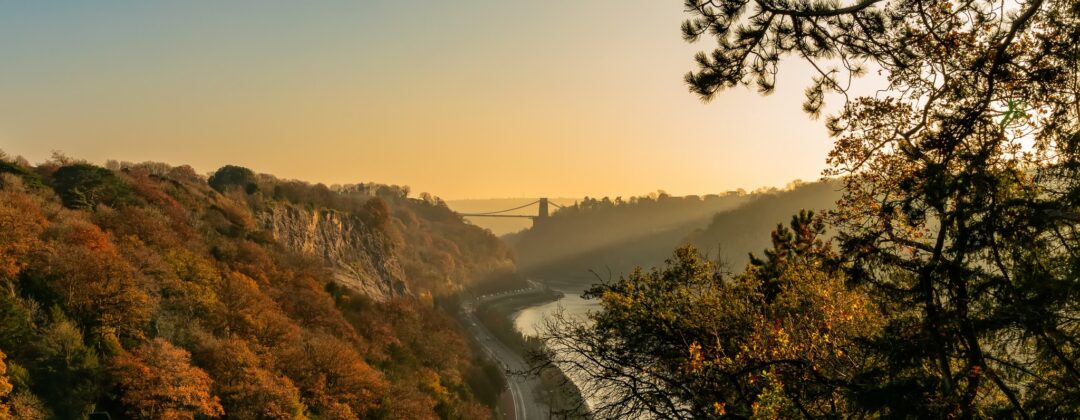 Sunrise view over a wooded river valley and distant suspension bridge, ideal for hiking near Bristol by train or bus