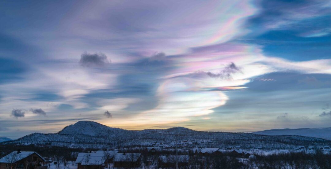 Daytime northern lights (nacreous clouds) over a snowy landscape in Finland at dusk