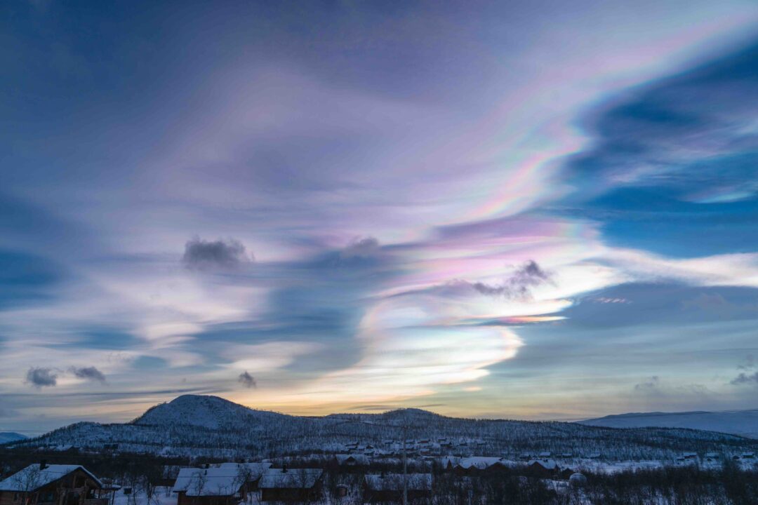 Nacreous, daytime northern lights clouds over a wintry landscape at dusk