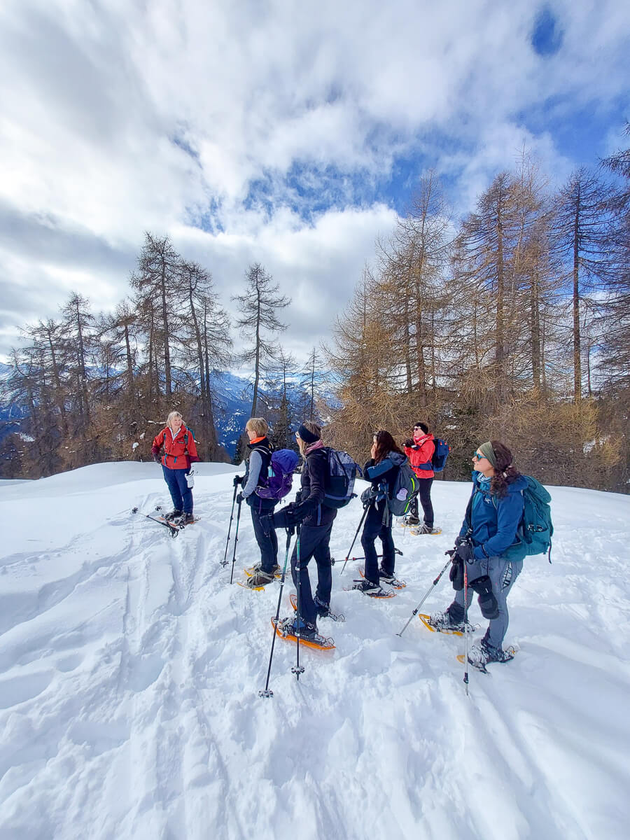 Women snowshoeing on a snowy mountain trail through a winter forest under a cloudy sky