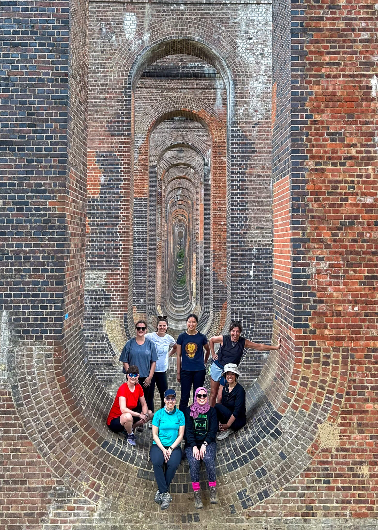 Women posing while walking inside a long arched brick tunnel walkway with patterned walls