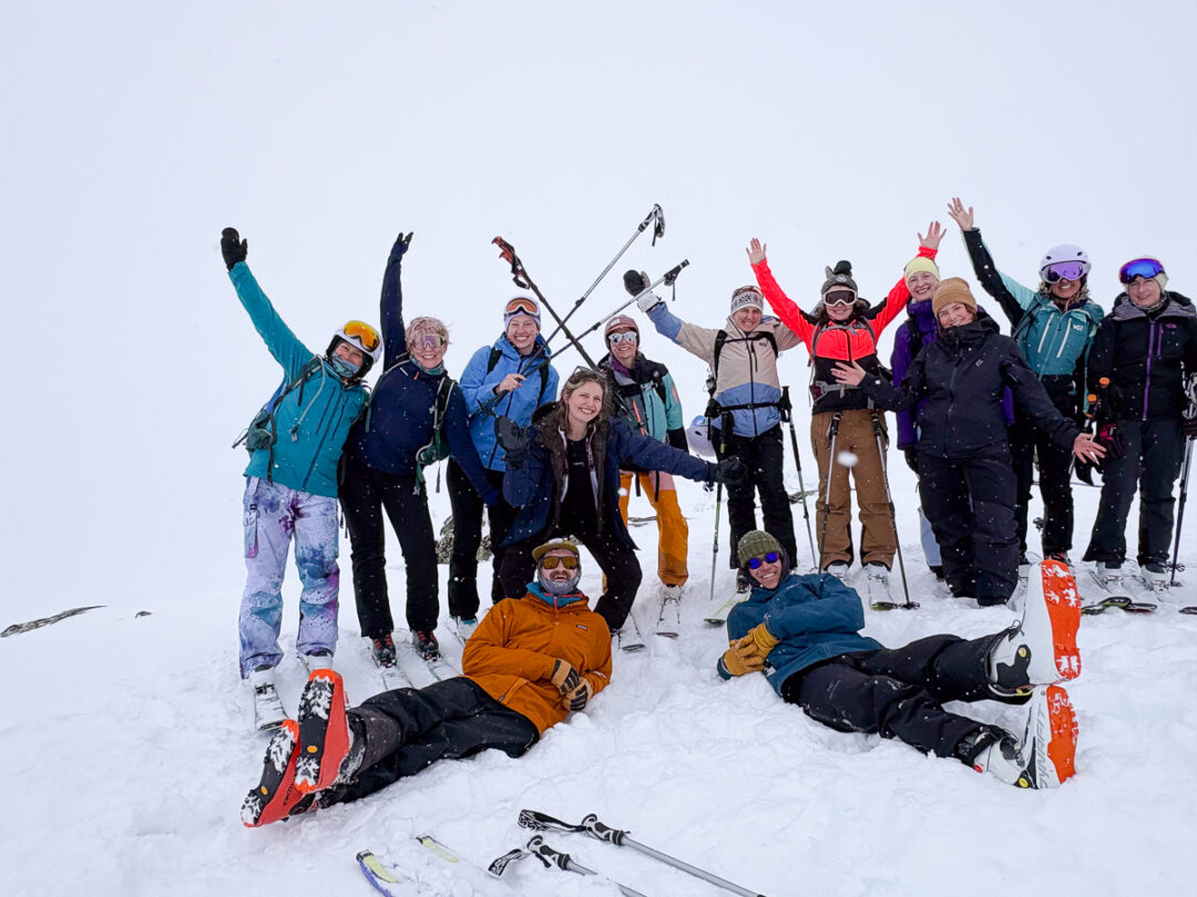 Group of women skiing on a snowy mountain, posing and waving with ski poles and skis