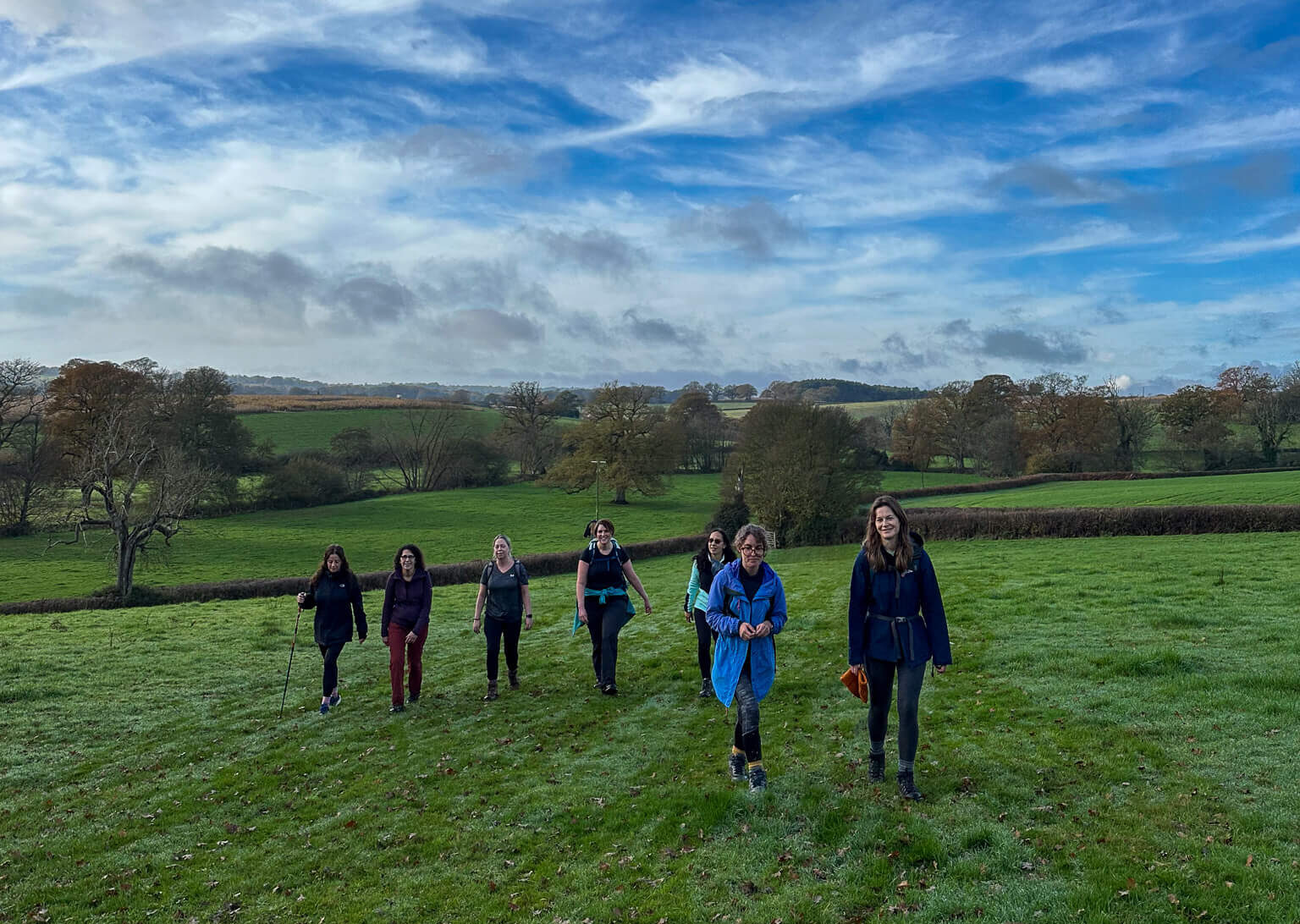 Group of women hiking across rolling fields in the Sussex countryside on a guided day hike.