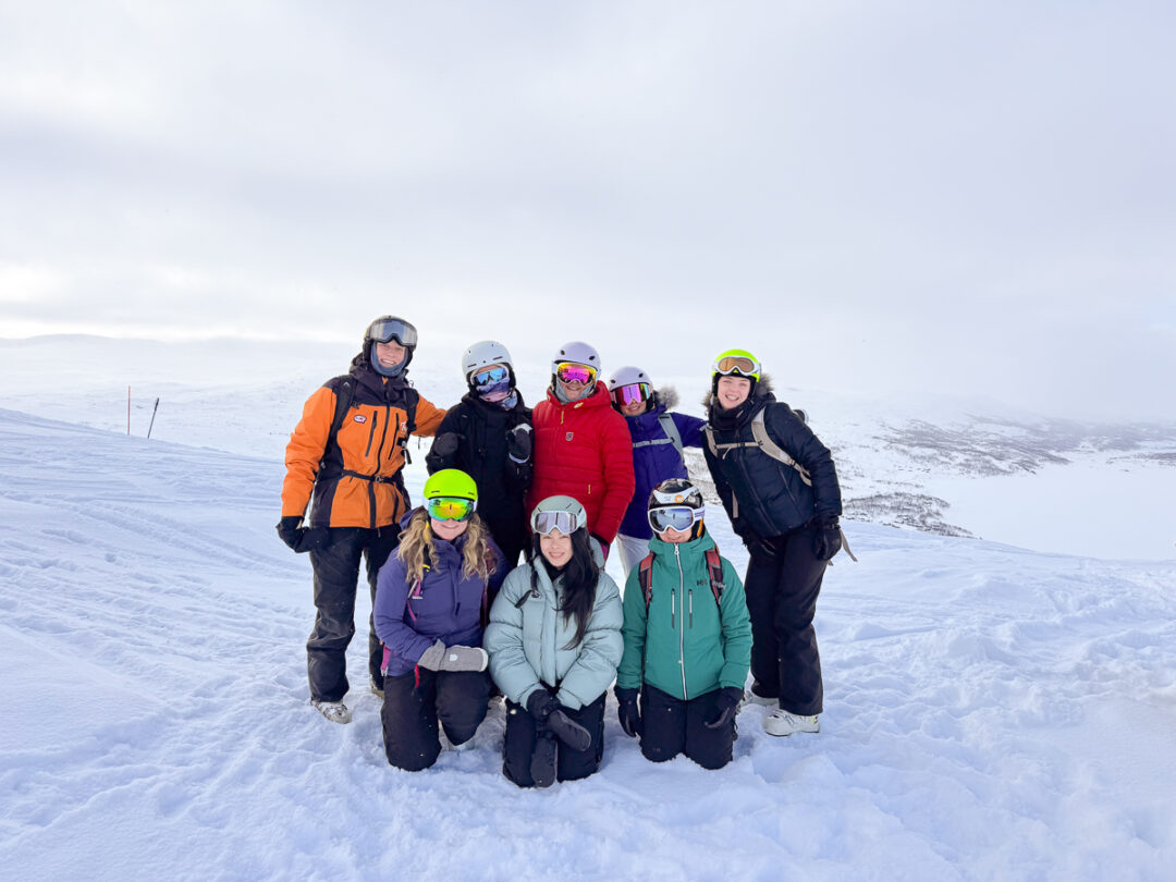 Women in ski helmets and winter jackets posing on a snowy mountain summit in Europe
