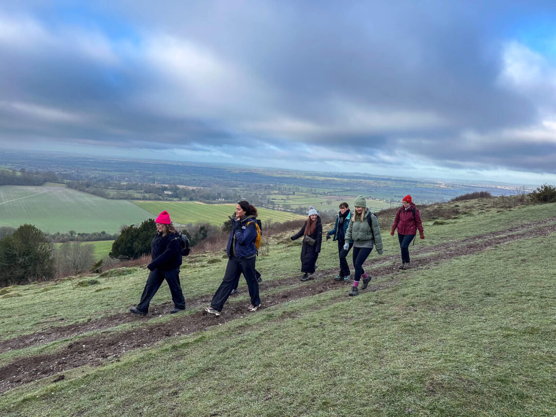 Women on a guided hike across grassy Chilterns hills with a valley view under a cloudy sky.