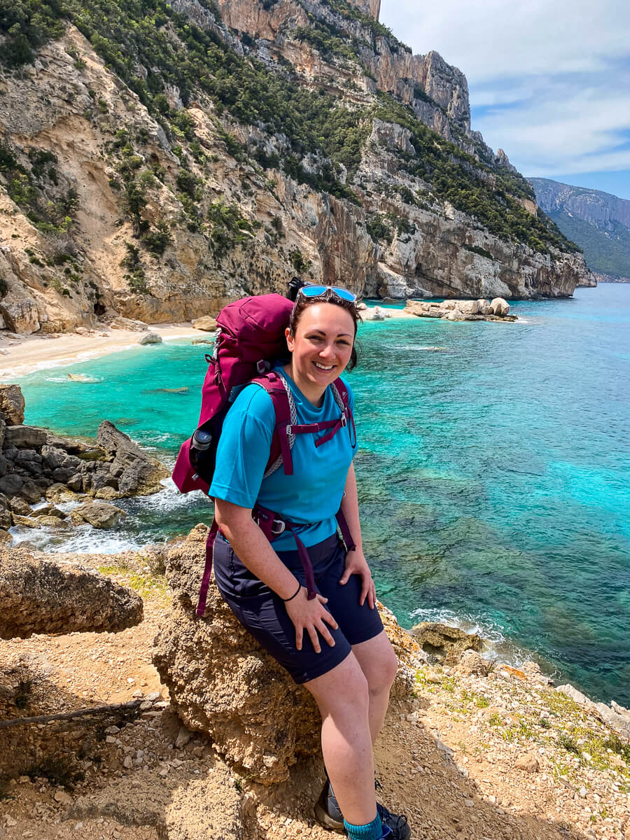 Woman hiking on a coastal cliff above a turquoise bay and rocky mountains