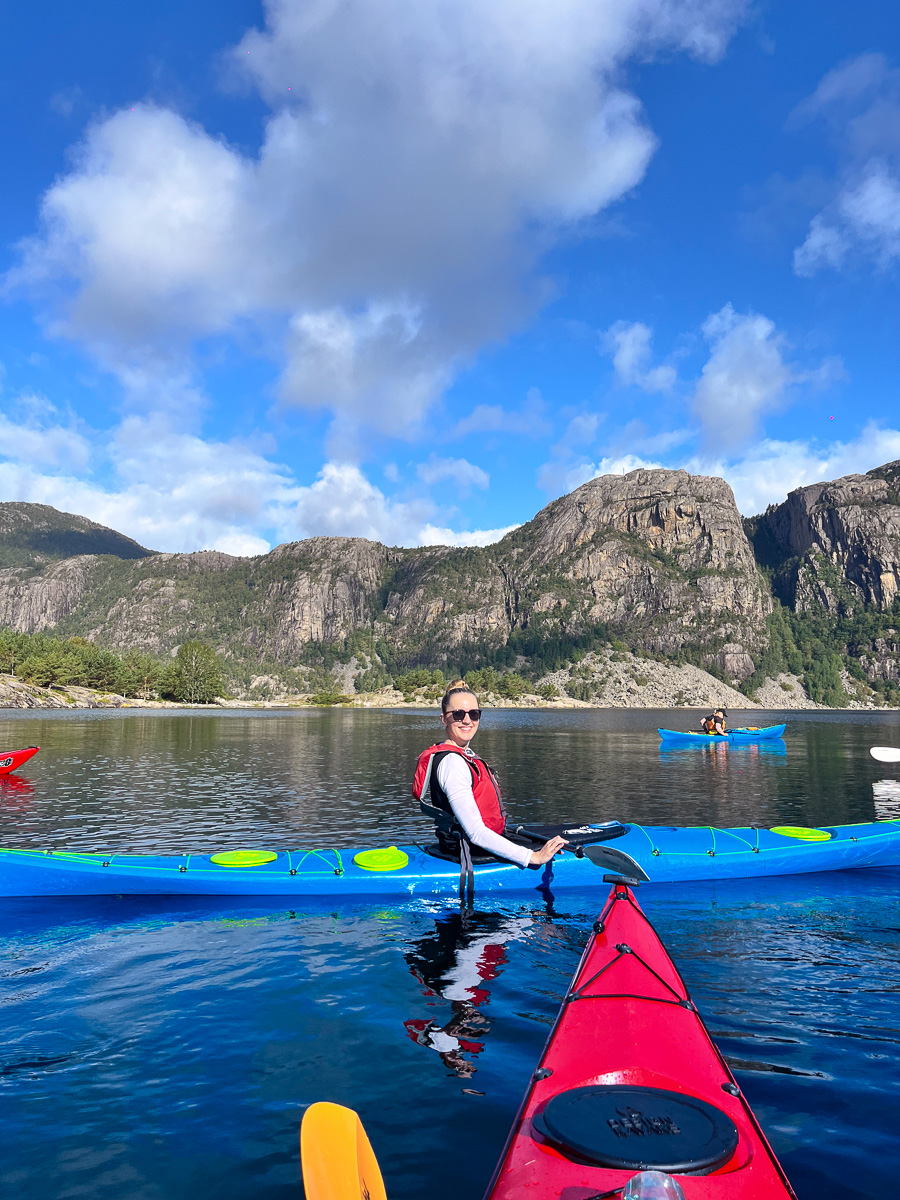 Woman kayaking on a calm lake in a blue sea kayak, with rocky mountains in the background