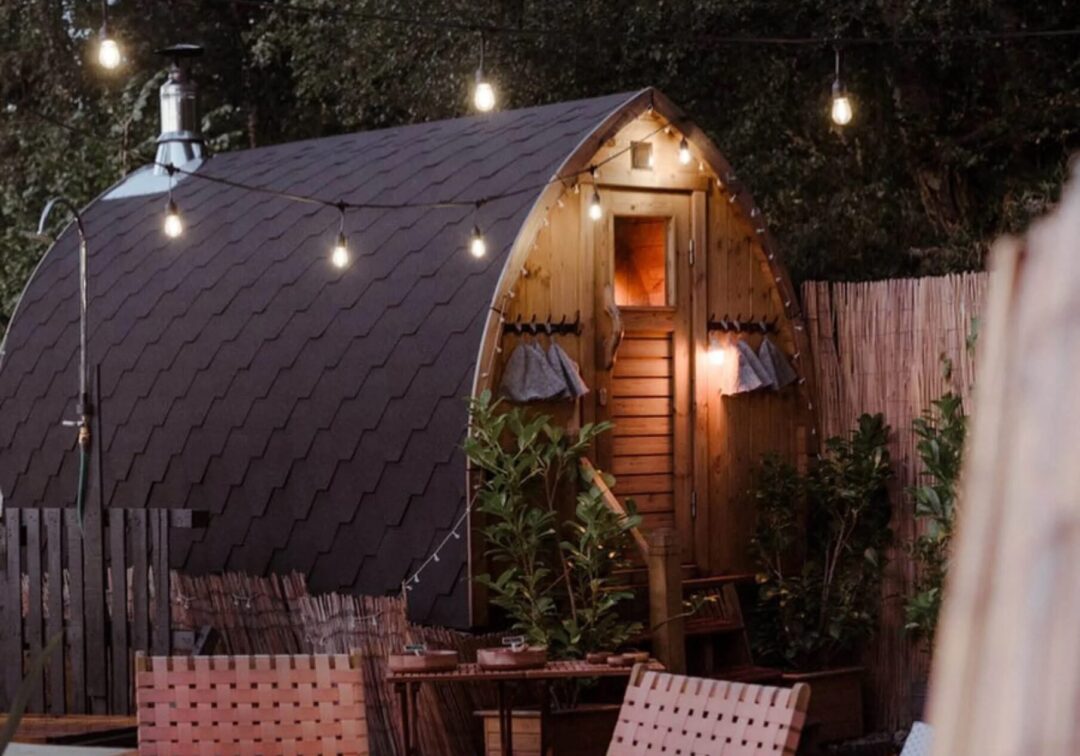 Outdoor wooden sauna hut with string lights at night in a garden yard