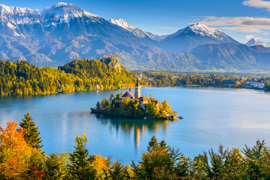 Serene lake with a small island church and alpine mountains in the background