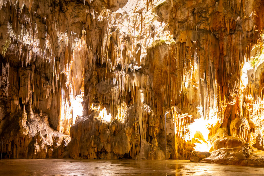 Cave interior with illuminated stalactites and stalagmites above a still underground pool
