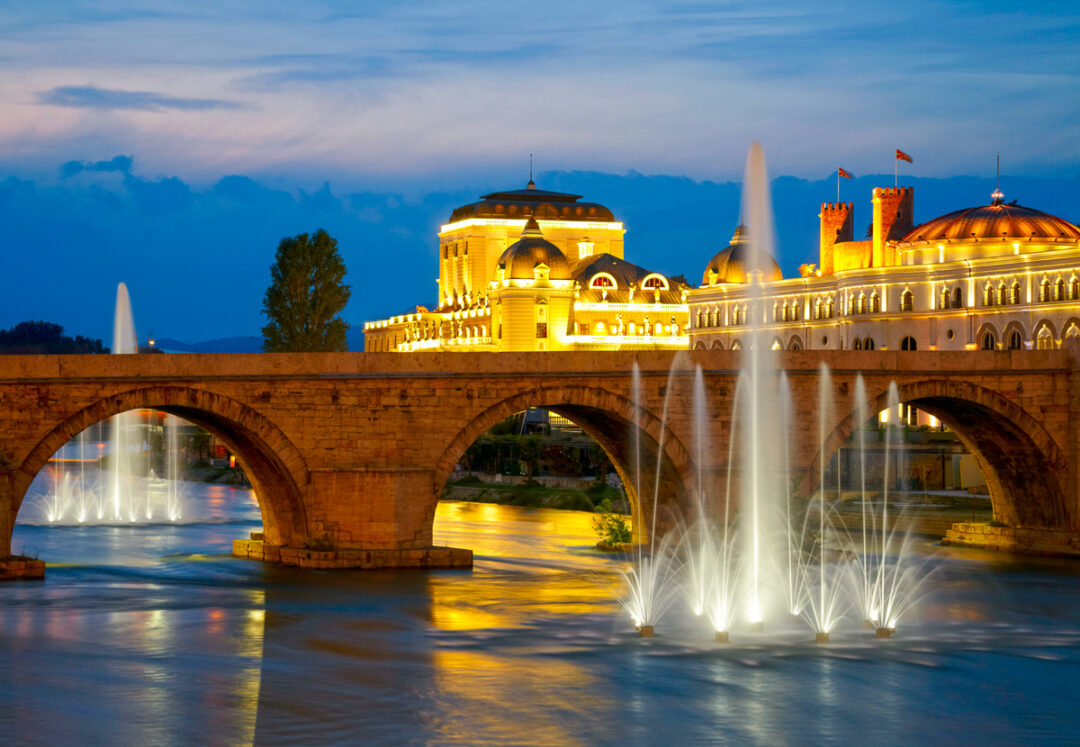 Fountains and illuminated bridge with a domed building at night in North Macedonia